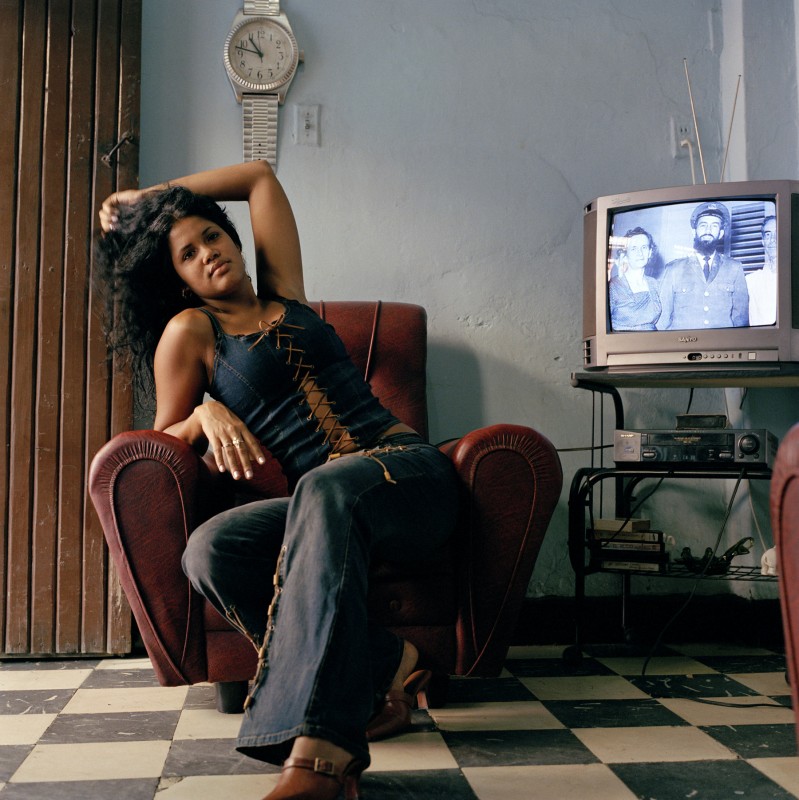 Woman posing in her living room, with Camillo Cienfuegos on the TV, October 2003
